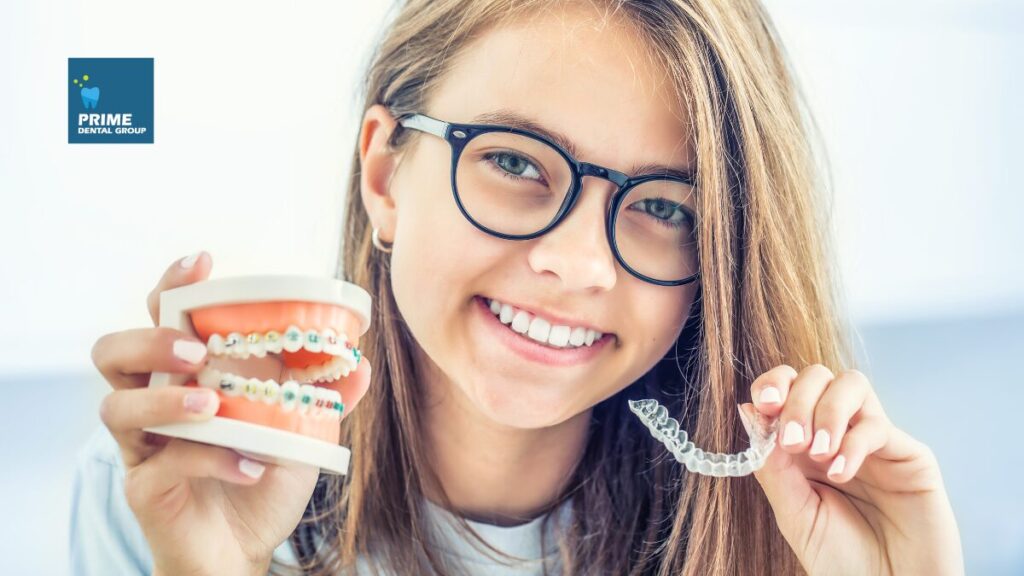 Smiling girl holding a dental model with braces in one hand and clear aligners in the other, showcasing orthodontic treatment options.