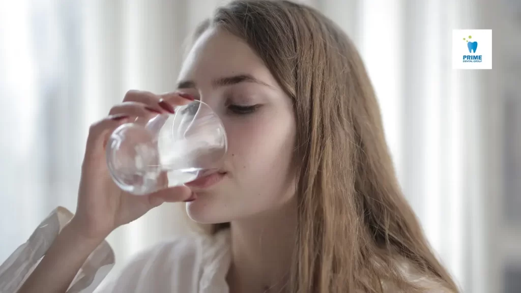 A woman drinking a glass of water, promoting hydration to improve saliva production and oral health.