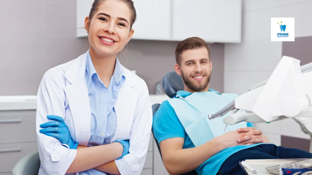 Dental professional in white coat smiling next to patient in examination chair during routine checkup