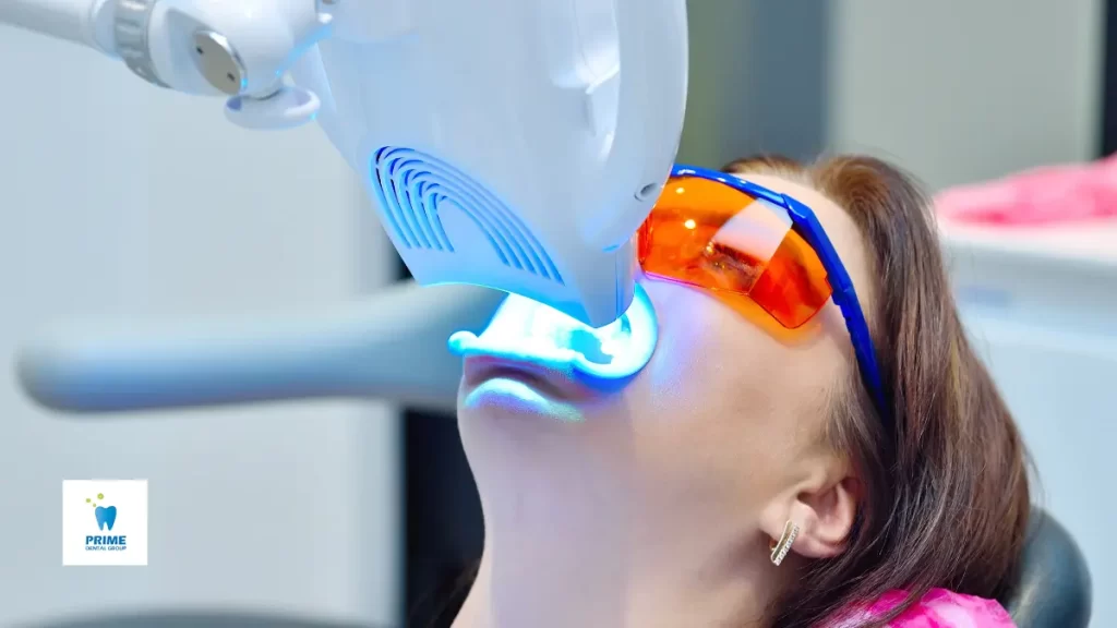 A patient undergoing professional teeth whitening with a blue LED light while wearing protective eyewear at a dental clinic.