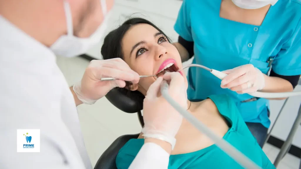 A woman receives a professional dental cleaning during her dental check ups, with two dental professionals using tools to clean her teeth.