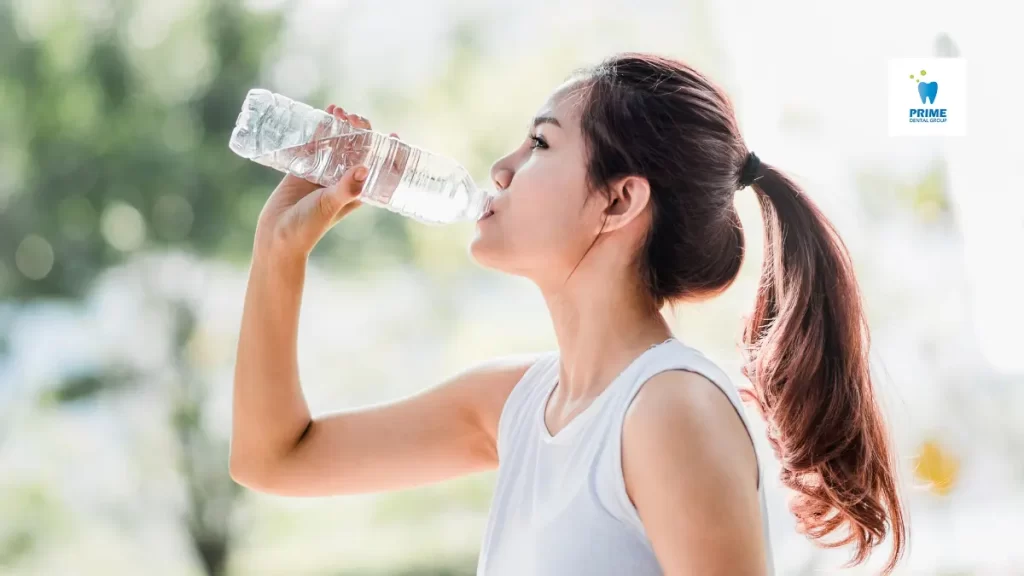 A young woman drinking water outdoors to stay hydrated and maintain fresh breath.