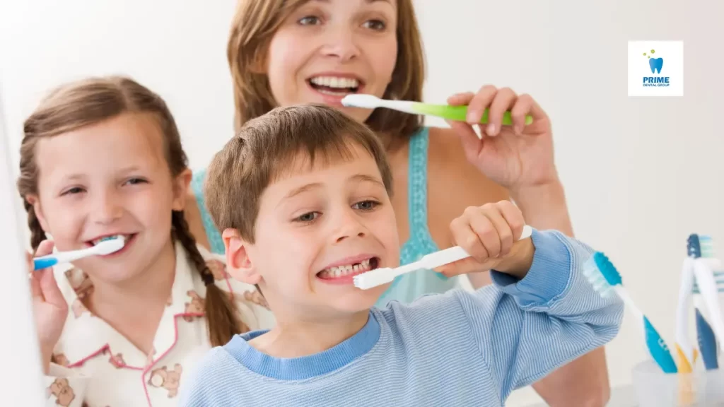 A mother and her two children brushing their teeth together in front of a mirror, promoting good oral hygiene habits.