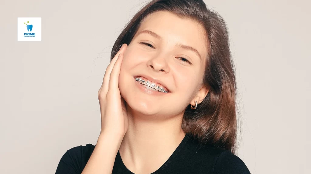 A smiling teenage girl with braces touches her cheek, showcasing confidence and the benefits of orthodontic treatment for a straighter, healthier smile.