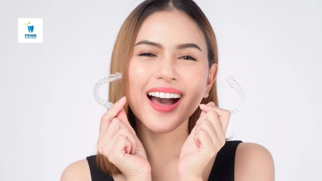 A smiling woman holds clear aligners, showcasing the benefits of Invisalign for a straighter, more confident smile without traditional braces.