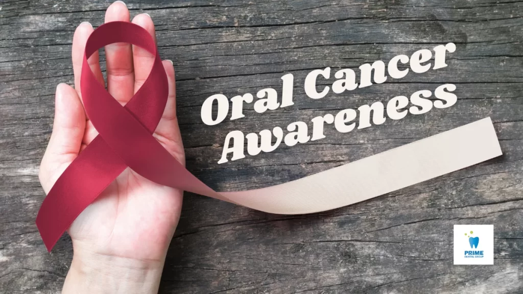 A hand holding a burgundy awareness ribbon for oral cancer on a wooden background.